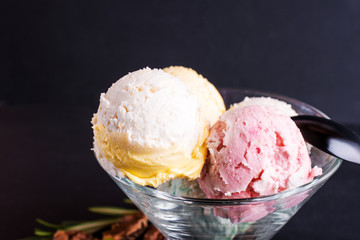 Three colorful balls of delicious ice cream, on a black background with nuts and a sprig of mint.