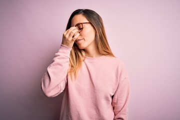 Beautiful blonde woman with blue eyes wearing sweater and glasses over pink background tired rubbing nose and eyes feeling fatigue and headache. Stress and frustration concept.
