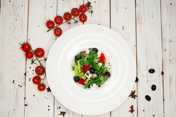 Greek salad of vegetables, cream cheese, olives and herbs served on a large white plate. Salad on a white wooden table.