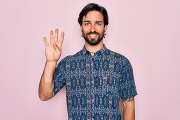 Fototapeta premium Young handsome hispanic bohemian man wearing hippie style over pink background showing and pointing up with fingers number four while smiling confident and happy.