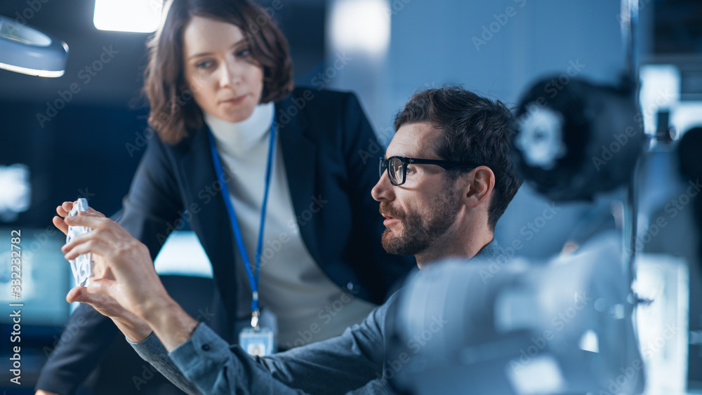 Poster Futuristic Machine Engine Development Engineer Working on Computer at His Desk, Talks with Female Project Manager. Team of Professionals Working in the Modern Industrial Design Facility