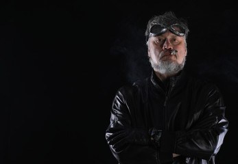 studio portrait of an old biker with a cigar on a black background