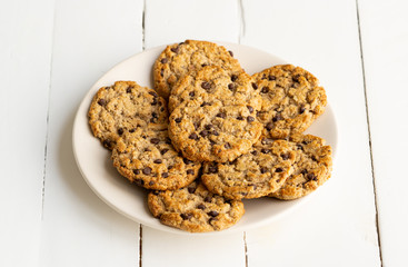 Chocolate chips cookies, biscuits, shortbread  in round plate on a white wooden table. Close up. Tasty crunchy dessert, breakfast, snack. Take away food. Bakery, tea, coffee house. Recipe, homemade. 