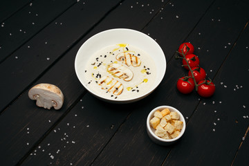 Delicate mushroom cream soup served on a dark white plate on a black wooden table, sprinkled with sea salt.
