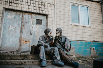 Couple in love sits in NBC protective suits and gas masks near building.
