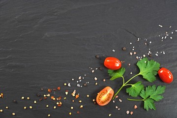 Rock salt, spices, parsley and cherry tomatoes on black granite stone with copy space. 