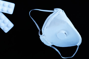 White ffp3 face mask with a valve and painkillers on a black background