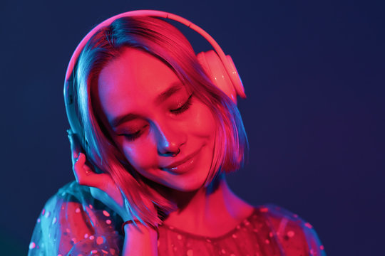 Mysterious hipster teenager listening to music with headphones. Portrait of millennial pretty girl with short hairstyle with neon light. Dyed blue and pink hair.