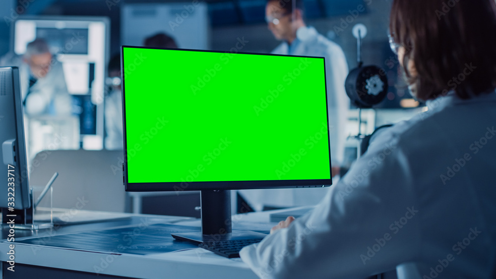 Aufkleber Over the Shoulder Shot: Female IT Scientist Uses Green Mock-up Screen Computer. In the Background Technology Research And Development Laboratory with Scientists, Engineers Working on High Tech Design