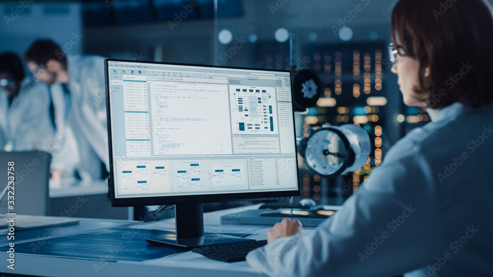 Poster Over the Shoulder Shot: Female IT Scientist Uses Computer Showing System Monitoring and Controlling Program. In the Background Technology Development Laboratory with Scientists, Engineers Working