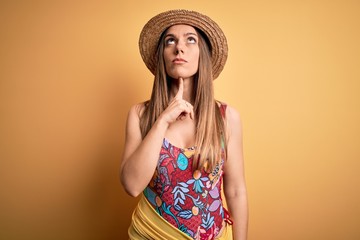 Young beautiful blonde woman wearing swimsuit and summer hat over yellow background Thinking...