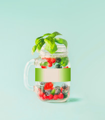 Detox fruit infused water in Mason jar with blank label mock up , flavored with herb leaves on table  at sunny turquoise blue background. Summer mood drinks. Healthy lifestyle