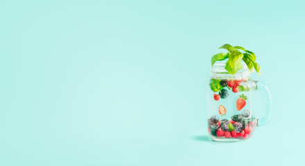 Berries detox fruit infused water in Mason jar flavored with herb leaves on table  at sunny turquoise blue background. Summer mood drinks and lifestyle. Healthy background