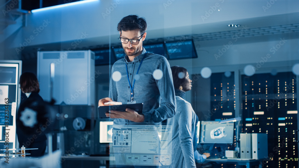 Fototapete In Technology Research Facility: Chief Engineer Stands in the Middle of Lab and Uses Tablet Computer. Team of Industrial Engineers, Developers Work on Engine Design Use Digital Whiteboard and Computer