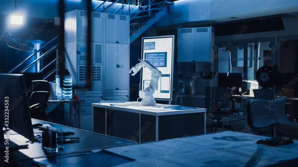 Poster In Industrial Robot Desing Research Laboratory: Robotic Arm Prototype Standing Illuminated on the Desk. In the Dark Background Various High Tech Devices, Computers, Digital Whiteboard and Blueprints