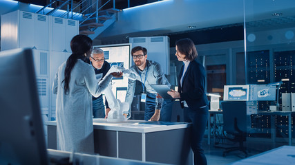 Engineers Meeting in Robotic Research Laboratory: Engineers, Scientists and Developers Gathered Around Illuminated Conference Table, Talking, Using Tablet and Analysing Design of Industrial Robot Arm