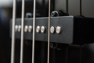 Close-up bass guitar pickups and strings. Musical instruments. Black guitar deck.