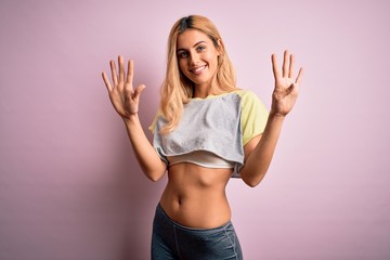 Young beautiful blonde sportswoman doing sport wearing sportswear over pink background showing and...