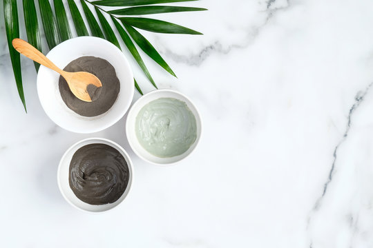 Natural organic SPA clay facial mask in bowls and tropical leaf on marble background. Face skin care and beauty treatment concept. Flat lay, top view