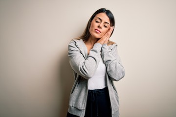 Fototapeta premium Young beautiful brunette sportswoman wearing sportswoman training over white background sleeping tired dreaming and posing with hands together while smiling with closed eyes.