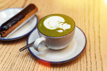 Matcha green in a white mug on a wooden table in a coffee shop next to a sweet dessert. Chocolate...