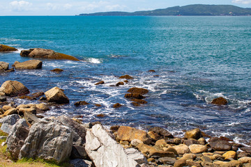 Fototapeta na wymiar Mar, rochas e céu azul com nuvens na Praia tropical de Ilhota em Itapema, Santa Catarina
