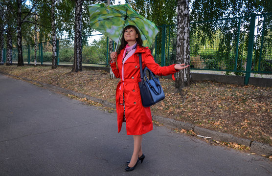 Beautiful portrait of a long hair brunette girl in red coat standing under green umbrella trying to find if rain