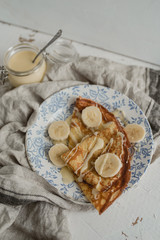 Crepe with condensed milk and a banana on a vintage plate and linen background. Tasty breakfast in rustic style. Top view.