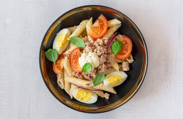 Tuna salad with pasta, tomato, egg in a bowl. Grey background. Top view, close up. Healthy, vegetarian restaurant dinner, lunch. Recipe, homemade. Italian, mediterranean. 