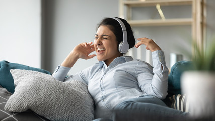 Excited Indian woman wearing wireless headphones singing popular song, having fun, happy smiling...