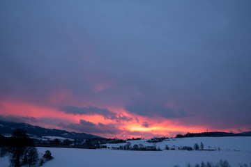 Red clouds at sunrise in winter in the mountains with several houses in the valley