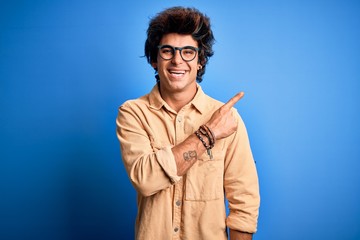 Young handsome man wearing casual shirt standing over isolated blue background cheerful with a smile of face pointing with hand and finger up to the side with happy and natural expression on face