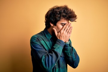 Young handsome man wearing casual shirt standing over isolated yellow background with sad expression covering face with hands while crying. Depression concept.