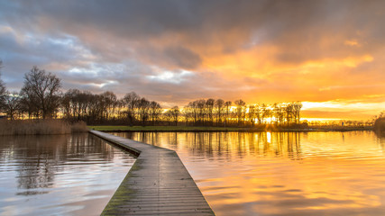 Fototapeta na wymiar Wooden walkway in lake under orange sunset
