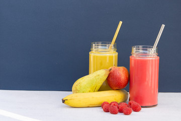 Banana and raspberry smoothie. Red and yellow. Glass, jar, metal straw. Some fruits around: apple, pears. Health, vegetarian, vegan breakfast, drink. No plastic, Ecology. Blue background, copy space.