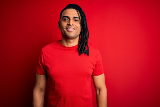 Young handsome african american afro man with dreadlocks wearing red casual t-shirt with a happy and cool smile on face. Lucky person.