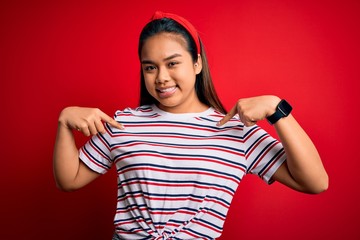 Young beautiful asian girl wearing casual striped t-shirt over isolated red background looking...
