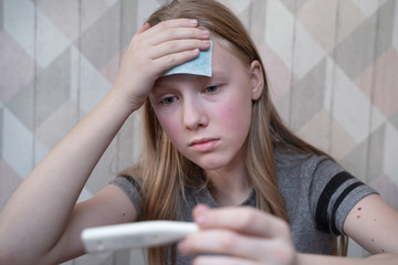 Naklejka premium a teenage girl with a patch on her forehead measures the temperature with an electronic thermometer