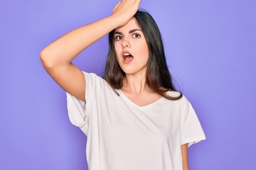 Young beautiful brunette woman wearing casual white t-shirt over purple background surprised with...