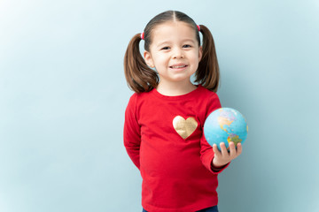 Portrait of a pretty little girl with ponytails holding a globe with a smile against a blue...