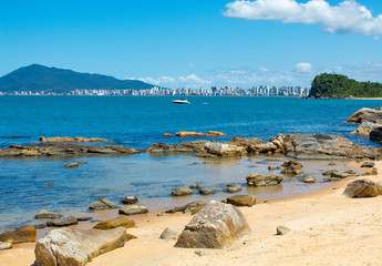Fototapeta na wymiar Lancha no mar, rochas e céu azul na Praia tropical de Ilhota em Itapema, Santa Catarina