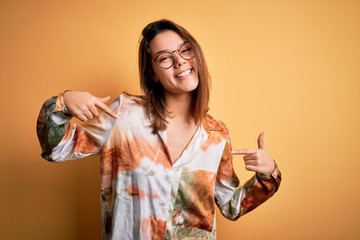 Young beautiful brunette girl wearing casual shirt and glasses over isolated yellow background...