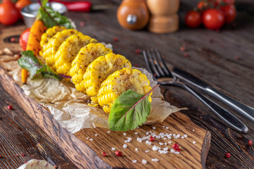 Grilled baked corn served with sauce and vegetables on a wooden board, selective focus
