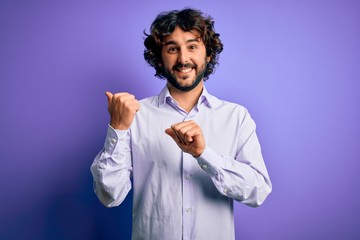 Young handsome business man with beard wearing shirt standing over purple background Pointing to the back behind with hand and thumbs up, smiling confident