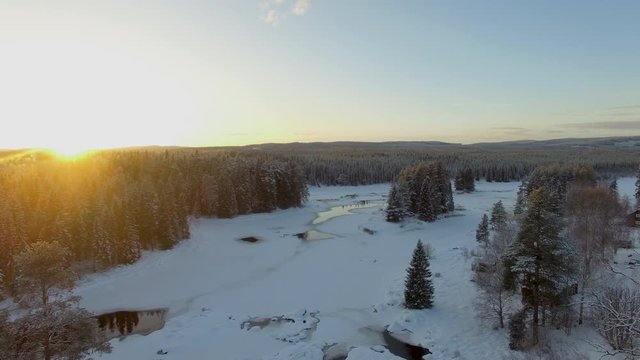 Cinematic aerial revealing a partially frozen river trough some trees during golden hour in 4K