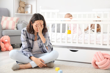 Young woman suffering from postnatal depression near bed with baby at home - obrazy, fototapety, plakaty