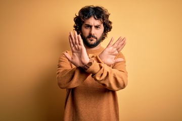 Fototapeta na wymiar Young handsome man with beard wearing casual sweater standing over yellow background Rejection expression crossing arms and palms doing negative sign, angry face