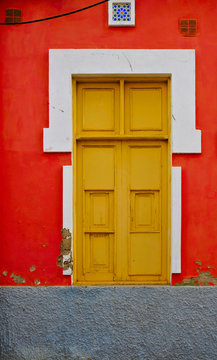 Old house with a window closed with brown wooden shutters in a red wall.