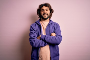 Young handsome sporty man with beard wearing casual sweatshirt over pink background happy face smiling with crossed arms looking at the camera. Positive person.