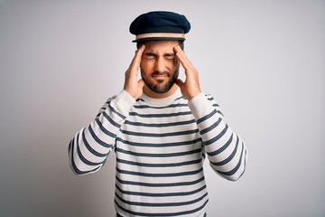 Young handsome sailor man with beard wearing navy striped uniform and captain hat suffering from headache desperate and stressed because pain and migraine. Hands on head.